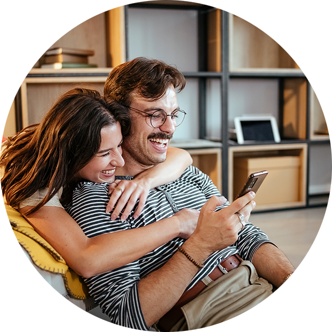 Couple embracing and laughing while looking at phone