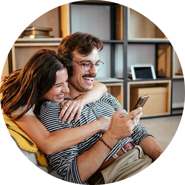 Couple embracing and laughing while looking at phone